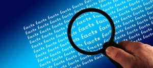 the word facts typed over and over again on a paper. The facts are so small the person needs to use a magnifying glass to see it.