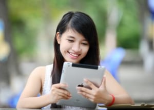 Girl at table outside smiling and looking at an ipad