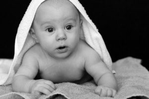 Baby on blanket with a towel over its a head and an expression of surprise