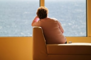 The back of a middle aged woman sitting in a lobby alone looking out a large window