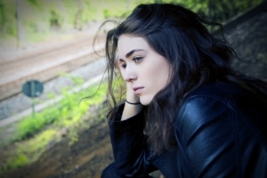 sad teen girl sitting on a hill near a road