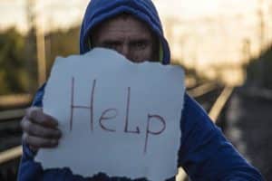 a young man with a hoody on is sitting on railway tracks with a sign that says help