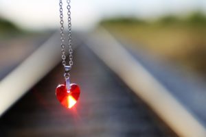 a heart pendant dangling from a chain with railway tracks blurred in the background