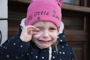 A little girl crying and rubbing her eye. She has a pink hat that says little cat