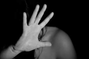 black and white photo of womans bare shoulder, her head is turned away so you can only see long dark hair and her palm is up and open as if deflecting a blow or angry words.