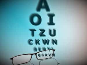 An alphabet eye chart that is blurry and a pair of glasses