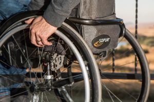 A partial side view of a man in a wheel chair and his hand on the wheel