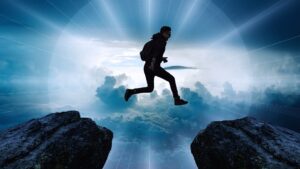 Boy with back pack jumping from one cliff to another. There are clouds in the back ground and rays of sun.