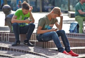 Two young men sitting outside looking at their cell phones.