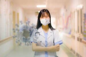A nurse with a mask standing in a hospital hallway and a covid molicule floating behind her