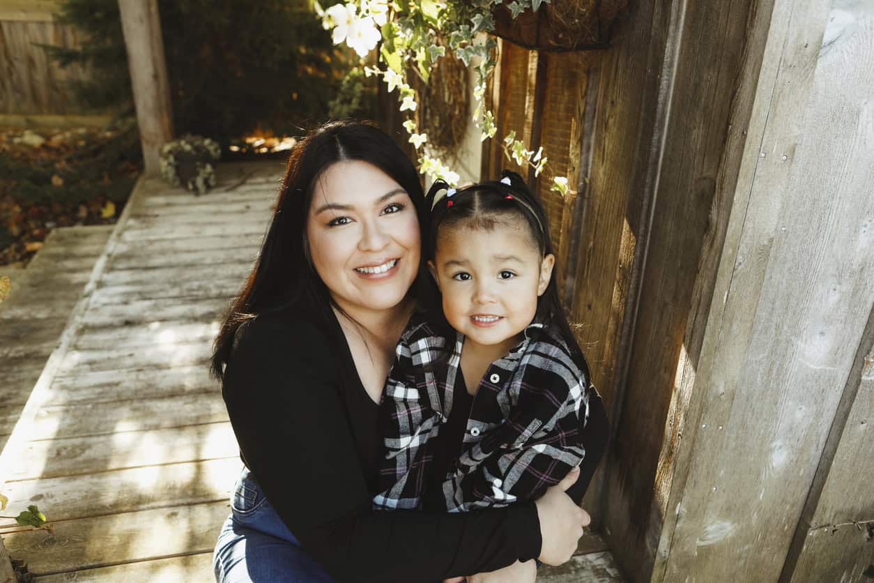 First nations mother kneeling beside her toddler daughter - both are smiling