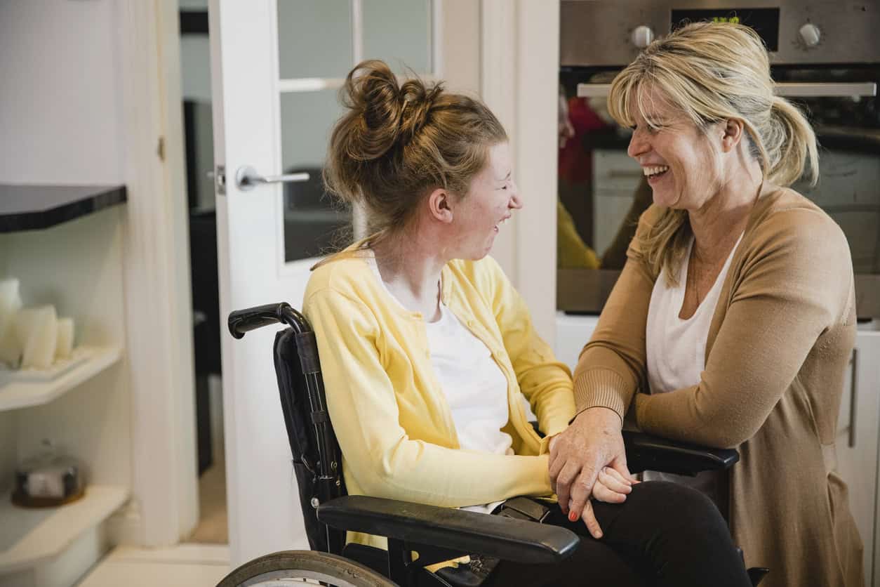 Mature mother is relaxing in the kitchen with her daughter who is in a wheelchair.