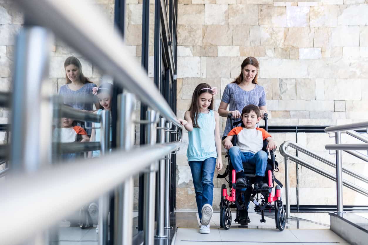 Mother pushing wheelchair with her son on it and sister walking next to him all leaving the clinic after physical therapy