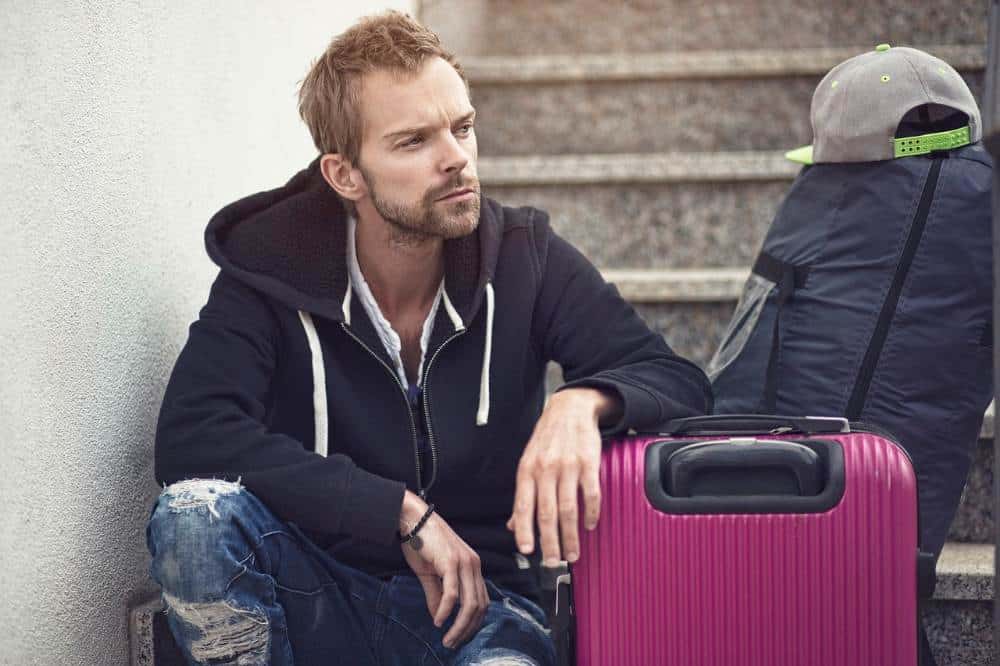 Young man sitting outside on cement steps leaning on a suitcase
