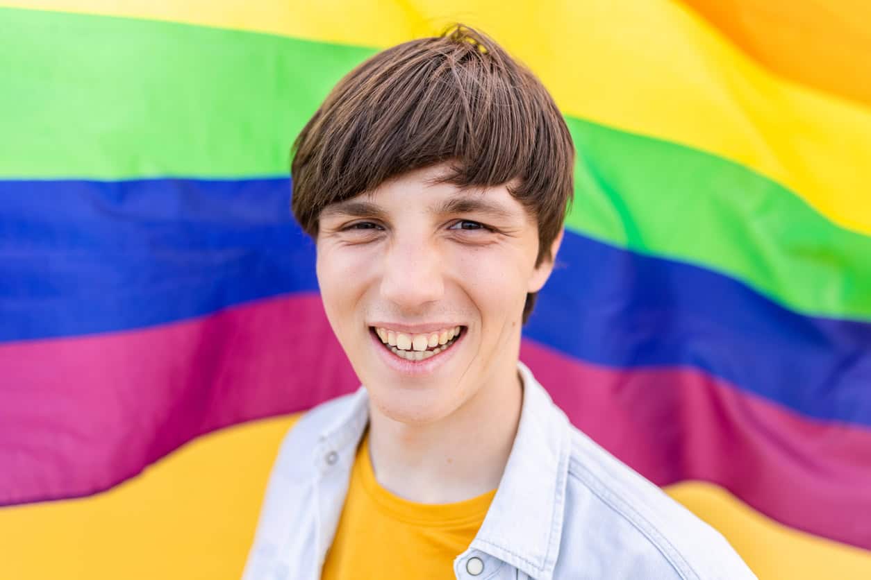 A young man standing in front of pride flag