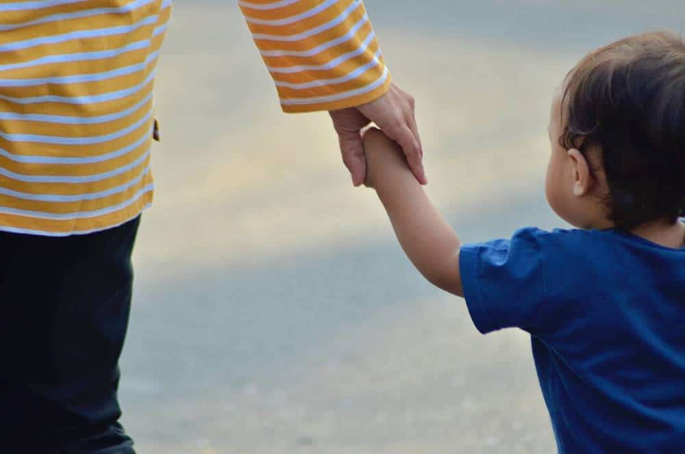 A mother walking with a toddler. She is holding his hand