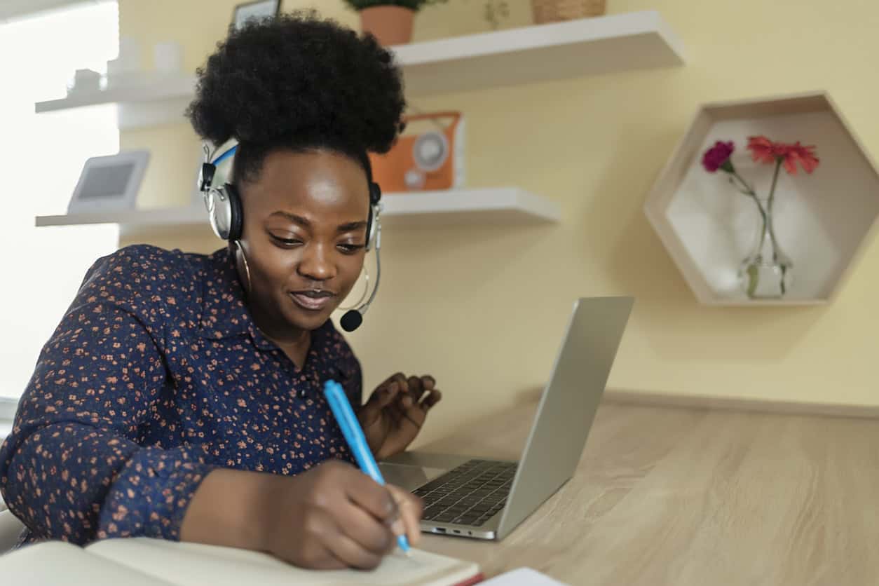 Smiling African American Female Employee in Wireless Earphones Talk on Video Call, Have Web Conference With Colleagues, Happy Ethnic Woman Worker in Headset Watch Webinar on Modern Laptop