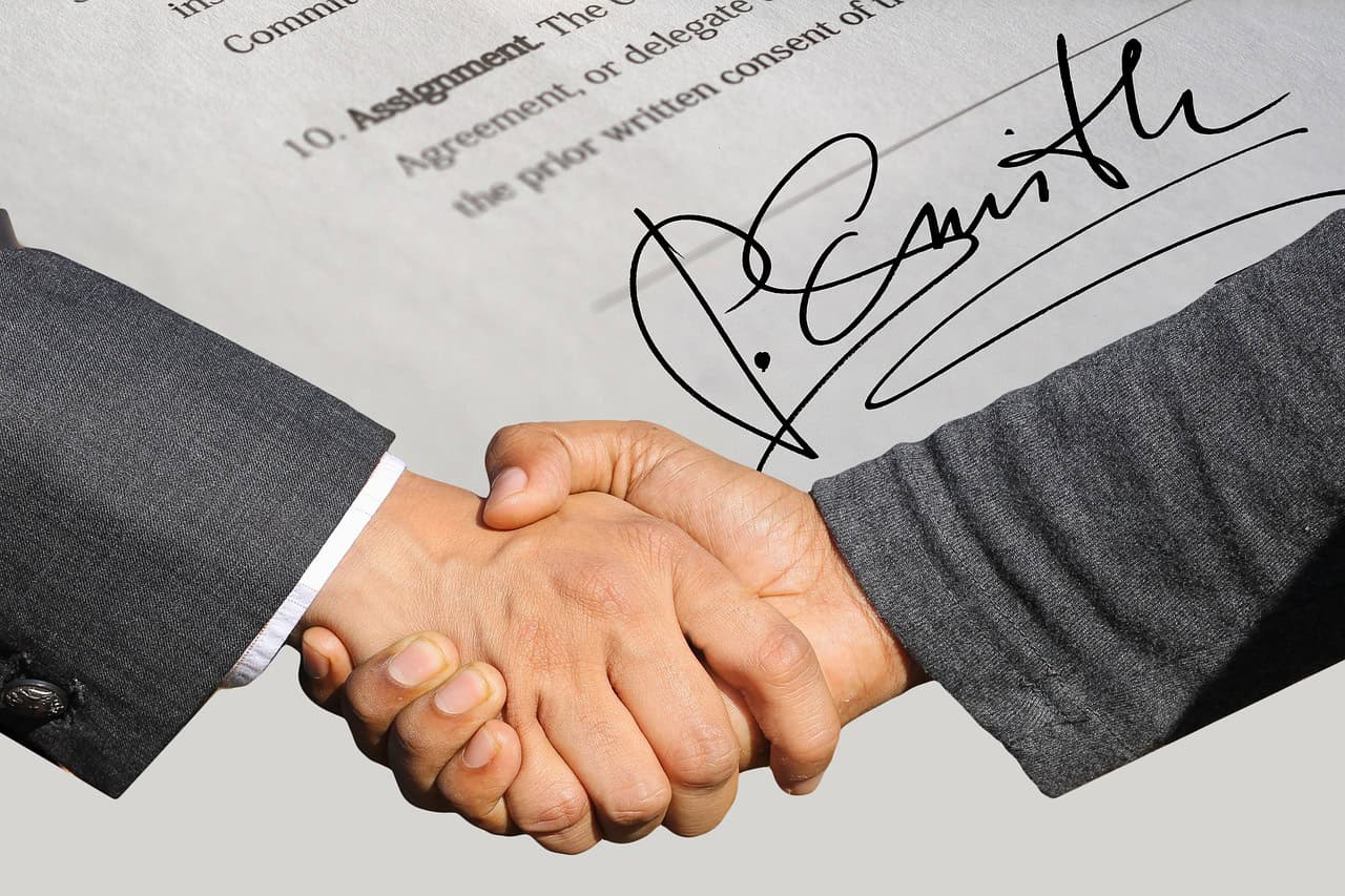 A signed contract and two people shaking hands