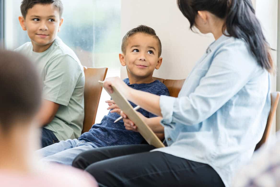 In the waiting room, an unrecognizable mother has her two young sons with her as she fills out paperwork.