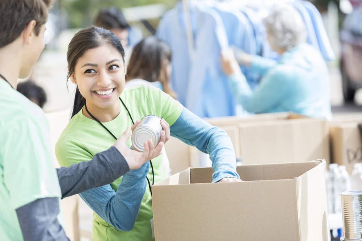Two young people volunteering at a program that provides clothes and food. They are packing a box with cans.