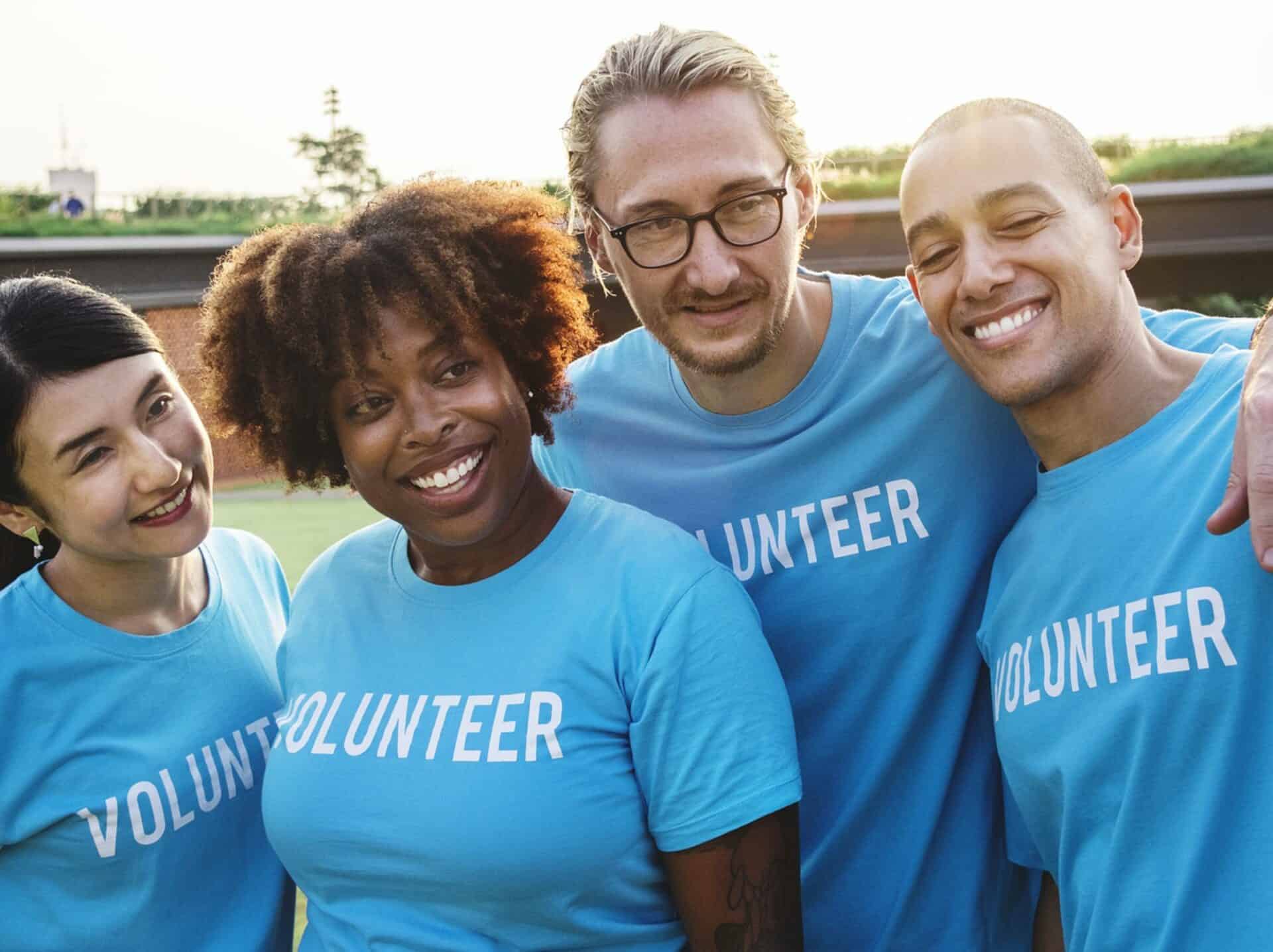 A group of 4 people standing together wearing blue t-shirts that say volunteer.