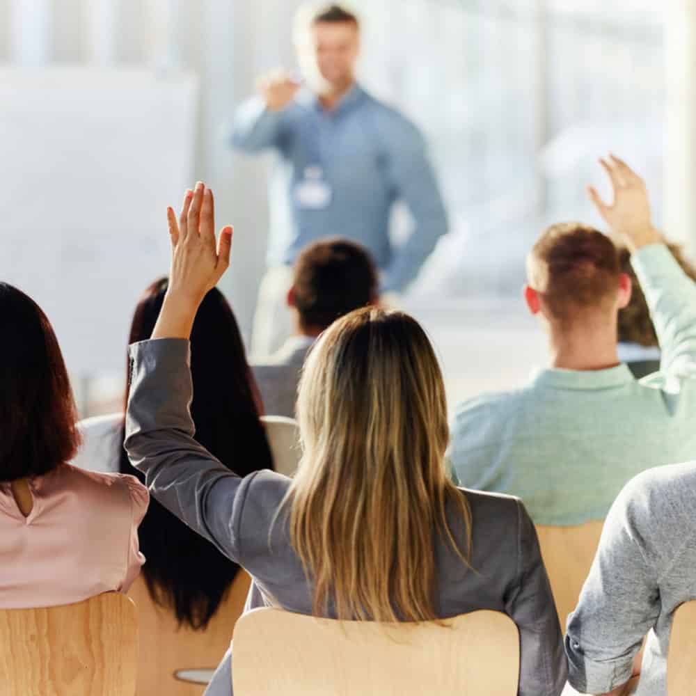 Rear view of a businesswoman raising her hand to ask a question on an education event in board room.